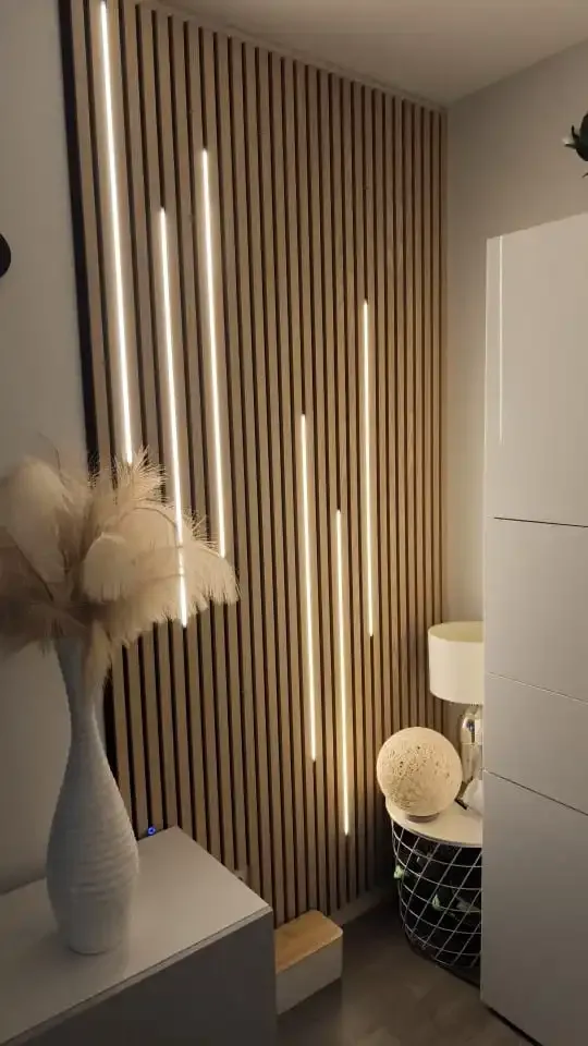Panel de lamas de madera en la pared con tiras de luz LED verticales integradas entre las lamas